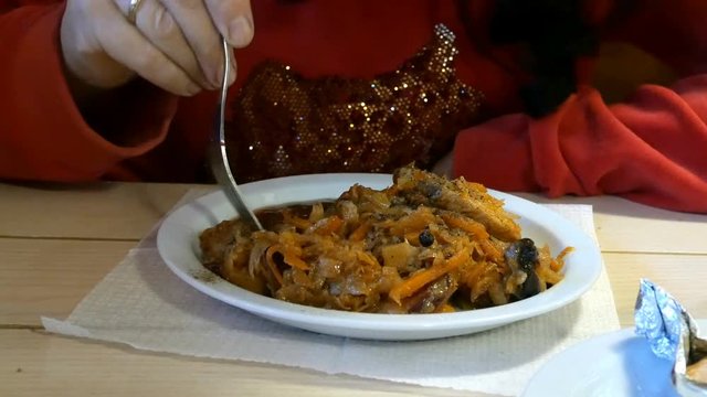 Person eats cabbage stew or bigus with meat, in a restaurant or cafe. With the help of a fork. Fragment with hands.