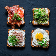 Breakfast sandwiches - avocado puree, fried egg, tomatoes, bacon, cream cheese, smoked mackerel grilled whole grain bread sandwiches. On a dark background, top view