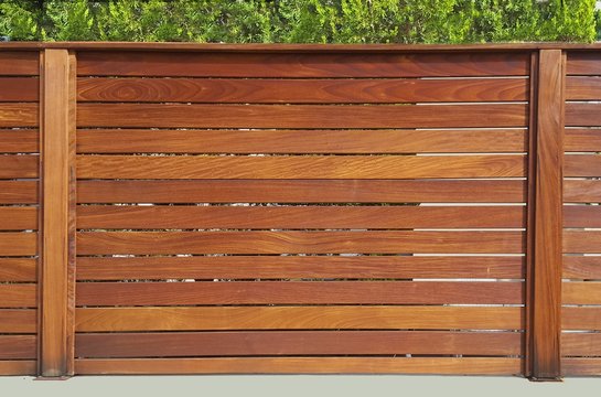 The fence around the house of wooden planks and wooden pillars, based on a concrete base