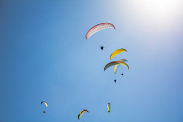 many paragliders on colorful parachutes in a clear blue sky with bright sunshine