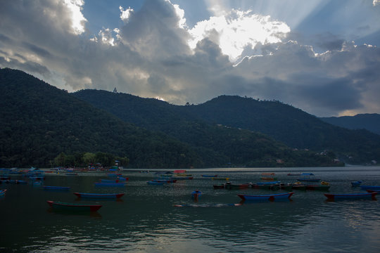 multicolored empty wooden boats on the lake against the background of green mountains and evening sunset sky with clouds