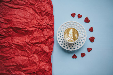 A cup of fresh flavored cappuccino coffee on a festive background with many hearts. Next to a red background there is a place for text. Celebration of Valentine's Day or Women's Day or other love