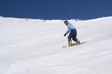Naklejka na ściany i meble Snowboarder riding on snowy ski slope at high winter mountains in sunny day