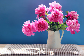 Pink peonies in a jug on a blue background.