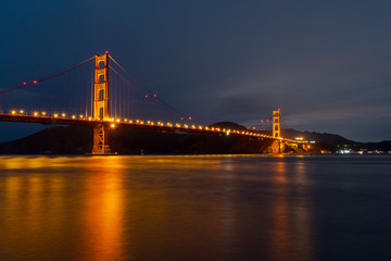 Nighttime view of Golden Gate Bridge reflected in the blurred water surface of San Francisco bay, California
