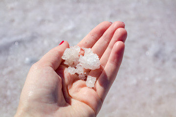 Female hand holding natural salt crystals on the background of a salt lake view from above