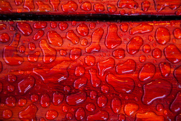 Figured drops of water on the surface of painted red boards bench on the streets 