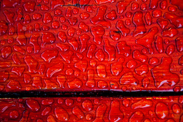 Figured drops of water on the surface of painted red boards bench on the streets