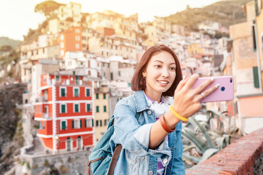 Young traveler tourist woman taking selfie on her smartphone in famous old italian village Riomaggiore, Cinque Terre, Italy
