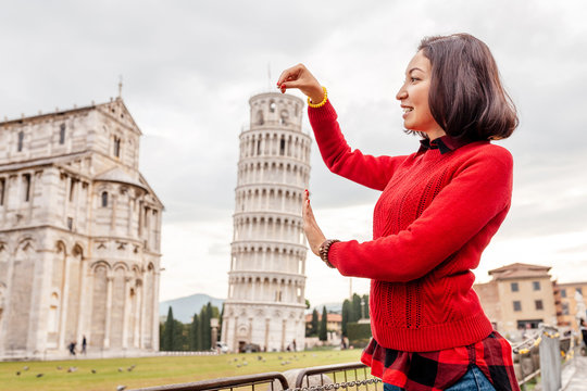 Young woman traveler making funny poses in front of the famous leaning tower in Pisa, Italy. Happy travel photos in Italy concept