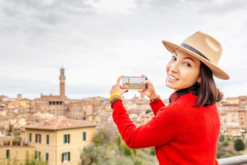 Traveler woman taking photo with her phone of the Siena city old town. Tourism in Tuscany and...
