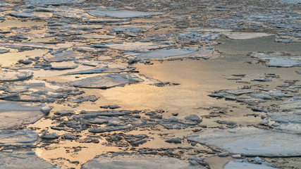 broken ice on a winter river with sunset sky reflection