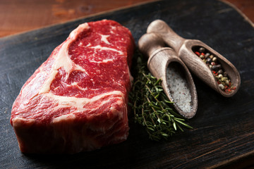 a piece of fresh marbled beef on a wooden background, with spices for cooking steak
