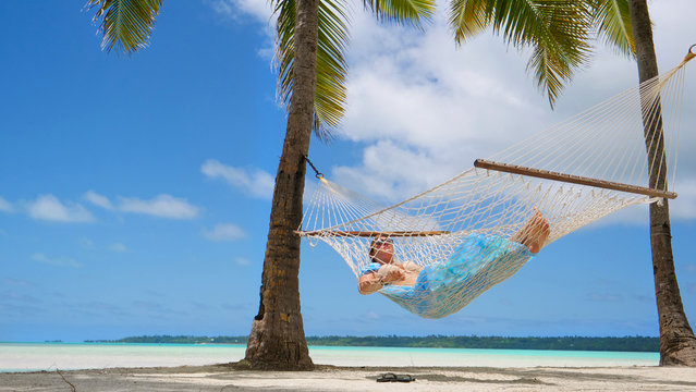 LOW ANGLE: Relaxed woman sleeps on the tropical beach in a swaying rope hammock