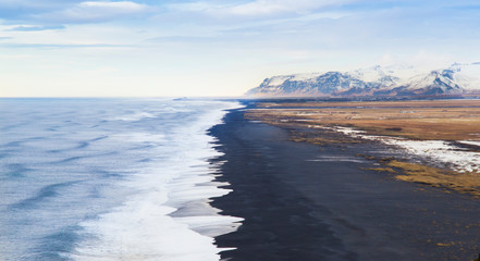 Reynisfjara black sand beach view from Dyrholaey, the 'door-hole', in Iceland at sunset with view of near glacier mountains