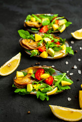 cooked mussels on a black concrete background with avocado, arugula, mango, tomatoes, lemon