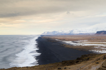 Reynisfjara black sand beach view from Dyrholaey, the 'door-hole', in Iceland at sunset with view of near glacier mountains