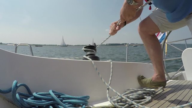 Footage of man using modern self-tailing winch on small recreational sailing boat here the line winched is a jib the handle is detachable to facilitate handling of the rope 4k high resolution quality