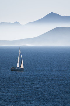 sea with sailboat and mountains of an islan