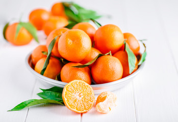 Tangerines (oranges, clementines, citrus fruits) with green leaves over wooden background with copy space.bowl of fresh mandarins