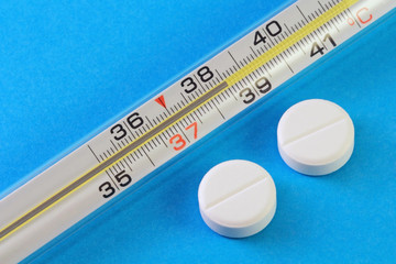 Medical mercury thermometer, showing high body temperature and two antipyretic pills. Antibiotic...