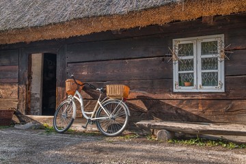 Stara, drewniana chata i rower z wiklinowymi koszami. Biskupin, Polska
