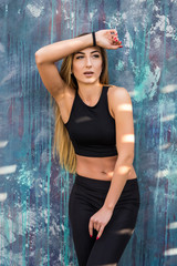 Outdoor shot of healthy fitness young woman standing against a street wall. Sportswoman relaxing after exercising outdoors.