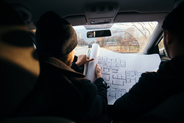 Two violent robbers sitting in a car looking at a blueprint of the building they want to rob while...
