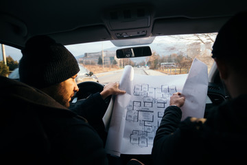 Two violent robbers sitting in a car looking at a blueprint of the building they want to rob while...