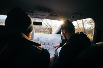 Two violent robbers sitting in a car looking at a blueprint of the building they want to rob while...