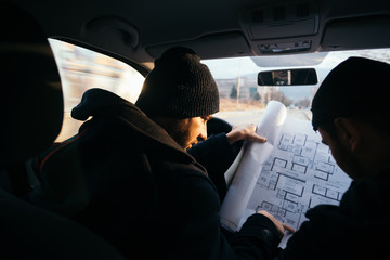 Two violent robbers sitting in a car looking at a blueprint of the building they want to rob while...