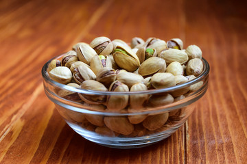 Pistachio nuts in a glass bowl on wooden background