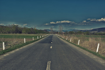 asphalt road through the green field and clouds on blue sky in summer day