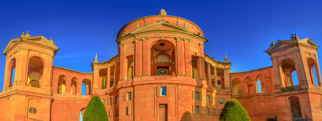 Wide angle panorama San Luca Holy Mary Sanctuary of Bologna at sunset. The Catholic cathedral of San Luca is located on the hills of Bologna city. Sunny with blue sky. Banner cityscape. © bennymarty