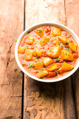 Indian food - Aloo curry masala. Potato cooked with spices and herbs in a tomato curry. served in a bowl over moody background. selective focus