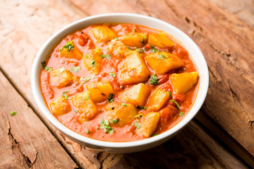 Indian food - Aloo curry masala. Potato cooked with spices and herbs in a tomato curry. served in a bowl over moody background. selective focus