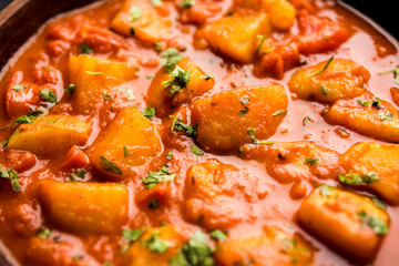 Indian food - Aloo curry masala. Potato cooked with spices and herbs in a tomato curry. served in a bowl over moody background. selective focus