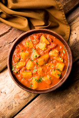 Indian food - Aloo curry masala. Potato cooked with spices and herbs in a tomato curry. served in a bowl over moody background. selective focus