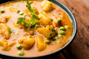 Indian Aloo Mutter curry - Potato and Peas immersed in an Onion Tomato Gravy and garnished with coriander leaves. Served in a Karahi/kadhai or pan or bowl. selective focus