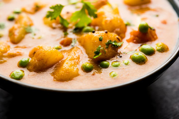 Indian Aloo Mutter curry - Potato and Peas immersed in an Onion Tomato Gravy and garnished with coriander leaves. Served in a Karahi/kadhai or pan or bowl. selective focus