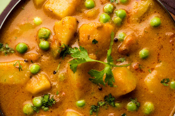 Indian Aloo Mutter curry - Potato and Peas immersed in an Onion Tomato Gravy and garnished with coriander leaves. Served in a Karahi/kadhai or pan or bowl. selective focus