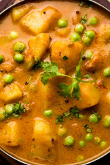 Indian Aloo Mutter curry - Potato and Peas immersed in an Onion Tomato Gravy and garnished with coriander leaves. Served in a Karahi/kadhai or pan or bowl. selective focus