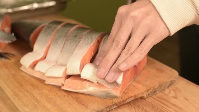 Close-up of female hands are cutting with a knife a large salmon on a wooden table of home cooking