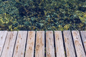 Fototapeta premium Wooden board empty over sea, can be used for display or present a product. Summer season. Empty perspective wooden planks over the reflection of green water, product display template.