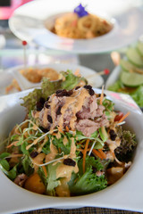 Tuna salad placed in a white circular ceramic dish topped with salad dressing and garnished with dried baby raisins