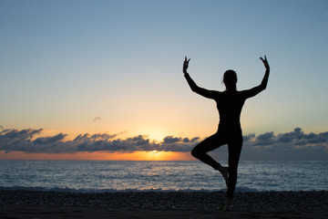 silhouette of woman doing yoga on the beach at sunset