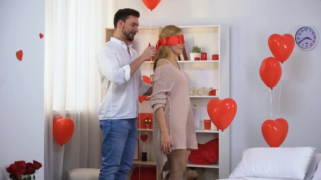 Man leading blindfolded with red ribbon lady into beautifully decorated room