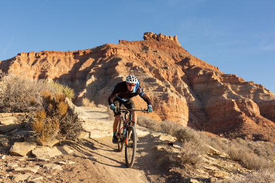 A young man rides a mountain bike over a sandstone ledge on the Jem trail in the desert of Southern Utah.