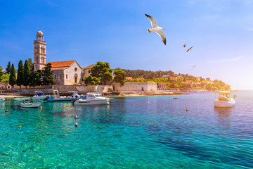 View at amazing archipelago with fishing boats in front of town Hvar, Croatia. Harbor of old Adriatic island town Hvar with seagull's flying over the city. Amazing Hvar city on Hvar island, Croatia. - obrazy, fototapety, plakaty