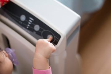 The baby's hand pressing the power button on the air purifier to clean up the polluted air.